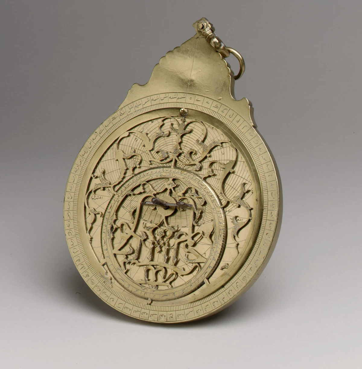 A brass planispheric astrolabe with engraved circular scales, a pierced star map and an ornate suspension at the top.